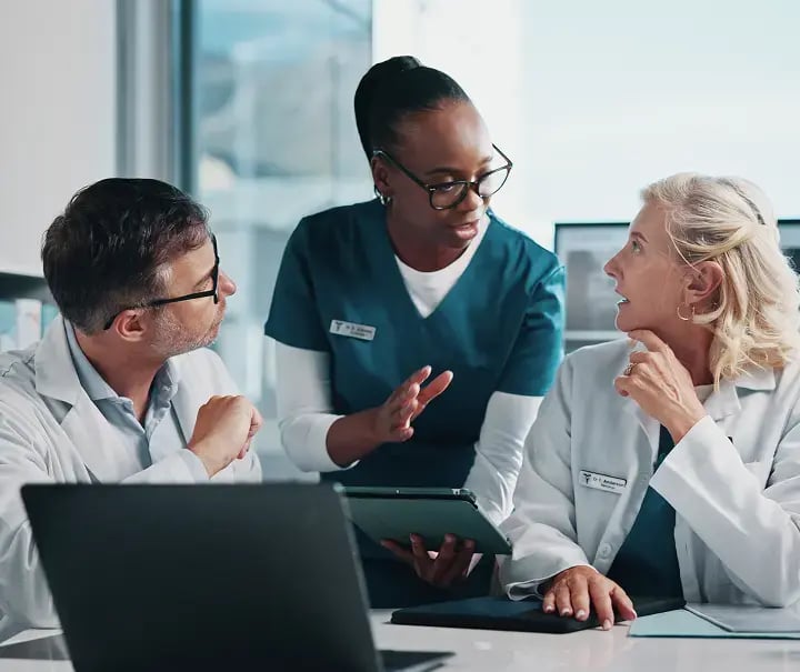 Equipo médico colaborando con una tableta y computadora en entorno hospitalario, simbolizando la integración radiológica con sistemas HIS para lograr continuidad clínica y máxima productividad mediante Aquila+ de IMEXHS.