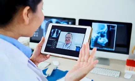 Profesional de la salud en videollamada con un especialista, utilizando una tableta para compartir estudios e imágenes médicas en línea mediante la plataforma Aquila+ de IMEXHS.