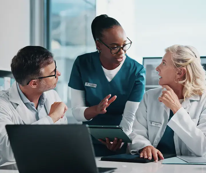 Equipo médico colaborando con una tableta y computadora en entorno hospitalario, simbolizando la integración radiológica con sistemas HIS para lograr continuidad clínica y máxima productividad mediante Aquila+ de IMEXHS.